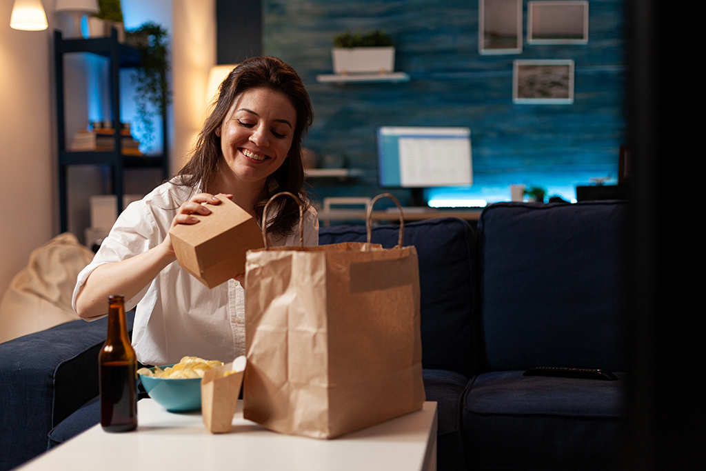 smiling cheerful woman unpacking tasting fast food home delivered sitting on couch